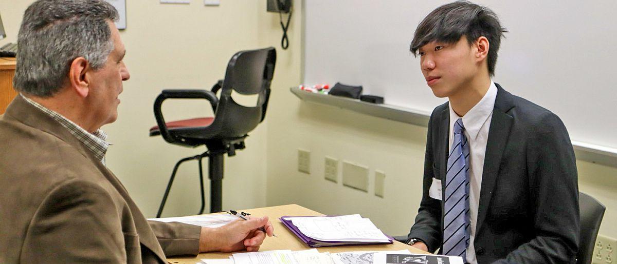 Female high school student shares laptop presentation during discussion with a contest judge.