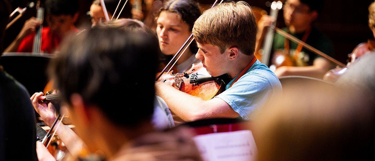 Image of students reading sheet music and playing violins.