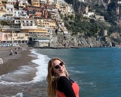 Claire Mulkey '23 standing on a beach with a mountainous city behind her.