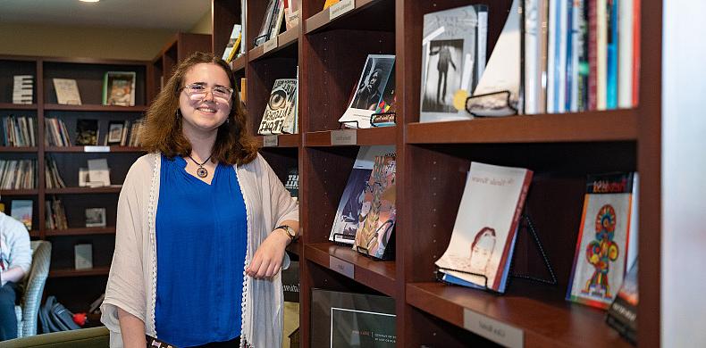 Emily Hizny st和s in front of a bookcase.